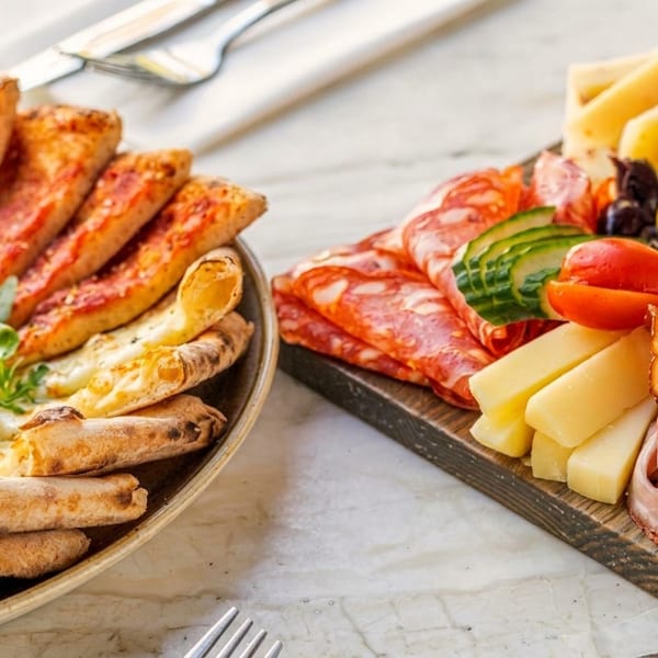A plate of pizza slices and a charcuterie board with meats, cheeses, and olives.