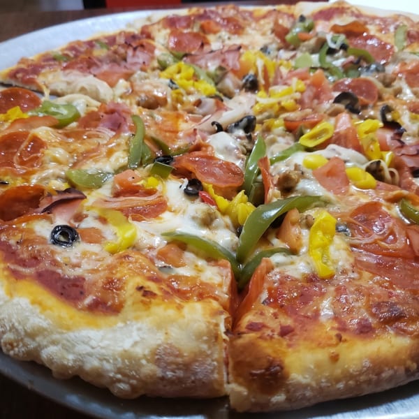 A large, freshly baked pizza with various toppings including pepperoni, ham, peppers, and olives.